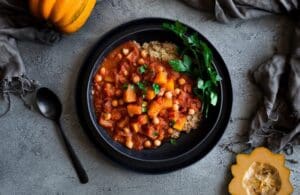 Plate with quinoa and chickpea vegetable stew garnished with parsley, black spoon and squash nearby