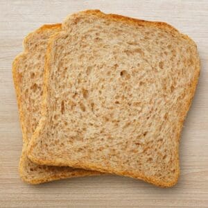 Two slices of light brown whole wheat bread on a wooden surface.