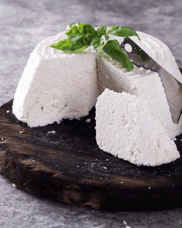 FRESH RICOTTA Soft white cheese on board with basil leaves and knife on gray surface.