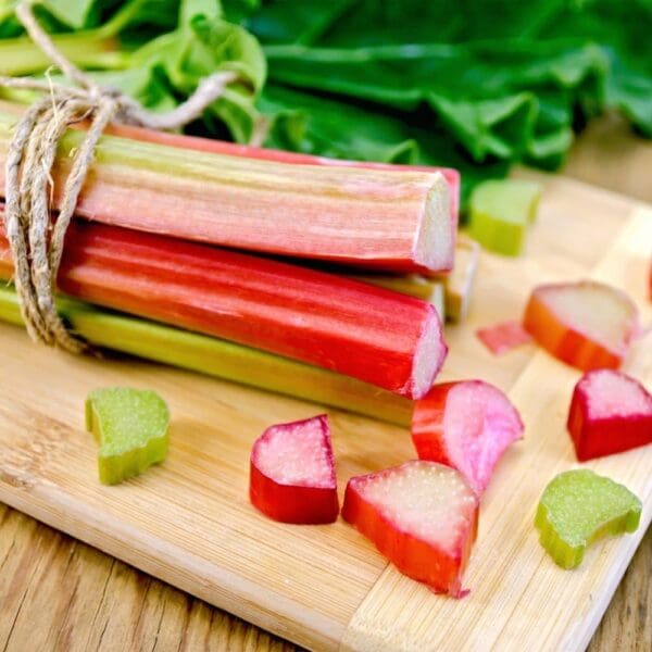 RHUBARB PACKS Fresh rhubarb stalks bundled with twine on cutting board, scattered slices, green leaves.