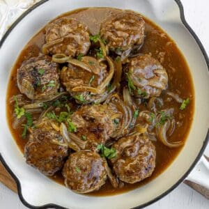 Glazed meatballs with herbs, pineapple, and sesame seeds in a rich sauce served in a bowl.