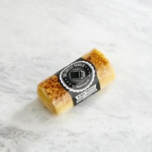 Small cylindrical block of Black Truffle Rebel Cheddar cheese, sealed, on a marble surface.