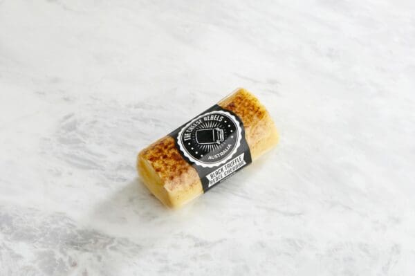 Small cylindrical block of Black Truffle Rebel Cheddar cheese, sealed, on a marble surface.