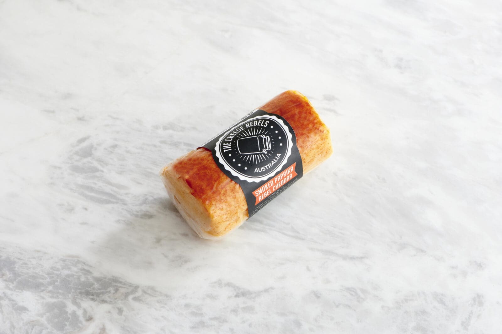 Cylindrical paprika cheese on plain marble background.