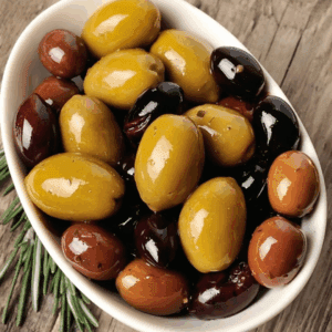 Bowl of assorted olives in green, brown, black with rosemary on wooden surface.