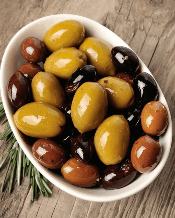 Bowl of assorted olives in green, brown, black with rosemary on wooden surface.