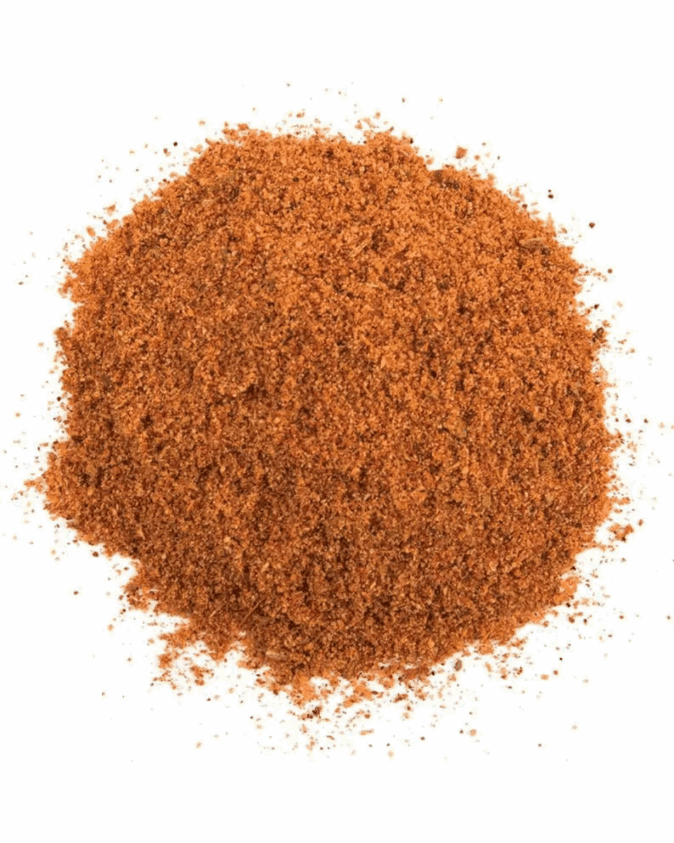 Pile of reddish-brown spice mix on a white background, coarse and granular texture.