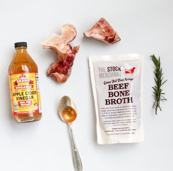 Apple cider vinegar, beef broth pack, beef bones, rosemary, and spoon on white background.