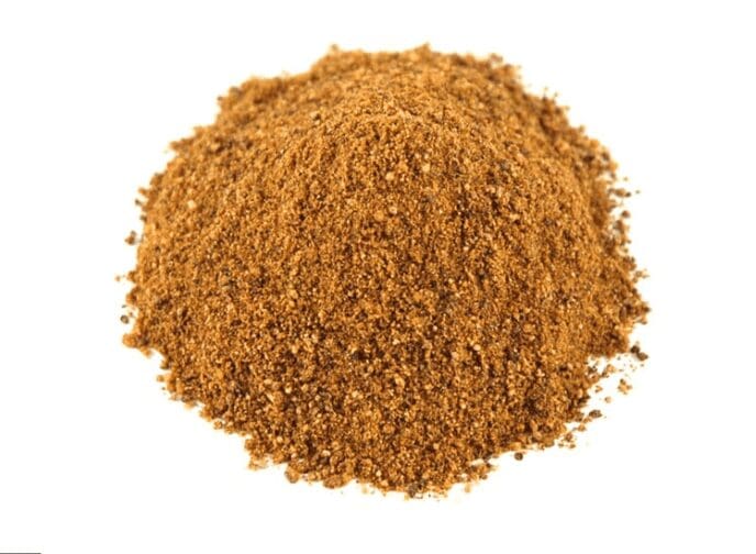 Brown, coarse ground spice pile on a plain white background, mixing granules and powder.