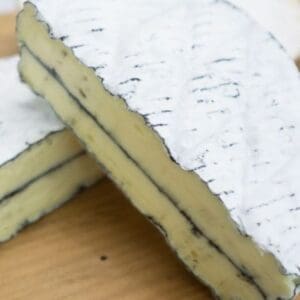 Cheese with white rind, thin ash line inside, on wooden surface.