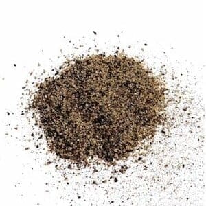 Pile of coarse black pepper granules scattered on white surface.
