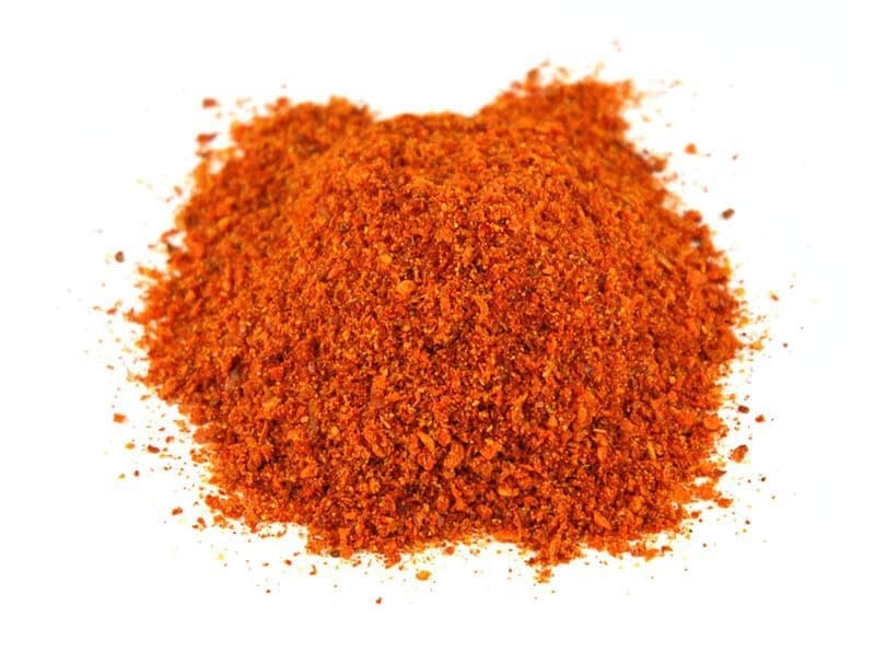 Small pile of coarse red-orange ground spice on white background.