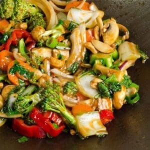 Colorful vegetable stir-fry with bell peppers, broccoli, mushrooms, carrots, onions, and nuts in sauce.