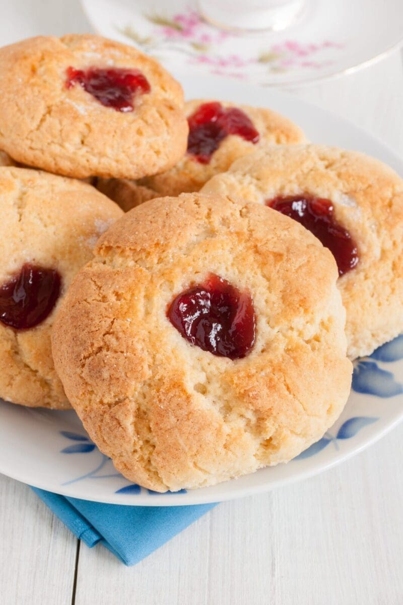 Cookies with crumbly texture and red jam center on a floral patterned plate.