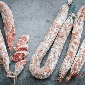 Cured sausages on gray surface, some sliced to show marbled insides and tied with strings.
