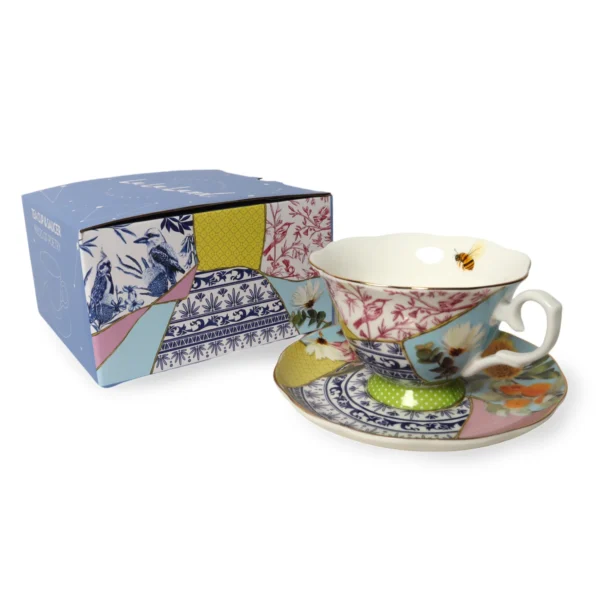 Decorative teacup and saucer with patchwork floral and bee design, next to matching box.