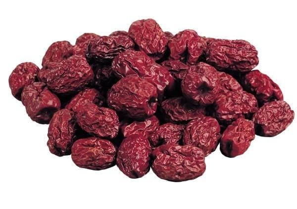 Pile of dried red fruits with wrinkled texture, resembling dates or jujubes, on plain background.