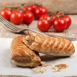 Flaky pastry with sausage filling on parchment, fork and cherry tomatoes in the background.