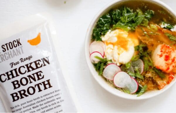 Free Range Chicken Bone Broth package beside a soup with greens, radishes, cream, and meat.