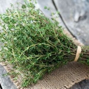 Fresh thyme bundle on burlap, rustic wooden background, small green leaves, thin woody stems.