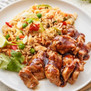 Plate with glazed chicken, fried rice with peas, red peppers, lime wedge, and cilantro.