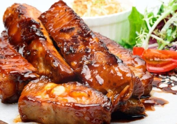 Glazed Ribs with Fresh Salad and Coleslaw Glazed meat ribs on a plate with salad, sliced tomatoes, and coleslaw in the background.