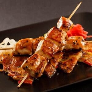 Skewered grilled chicken with glazed sauce, grilled vegetables, and pickled garnish.