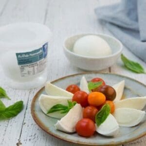 Plate with mozzarella slices, cherry tomatoes, basil; container and bowl in background.