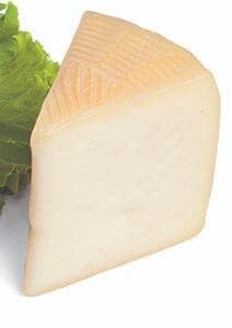 Wedge of pale cheese with textured rind on green lettuce background.