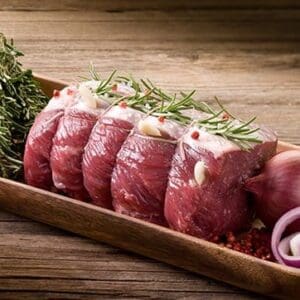 Slices of raw beef with rosemary, garlic, herbs, and red onion on a wooden tray.