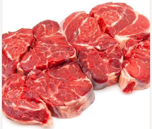 Raw beef steaks in a line on white surface, showing marbled textures, various red shades.