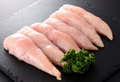 Slate platter with six raw chicken fillets and parsley garnish on dark background.