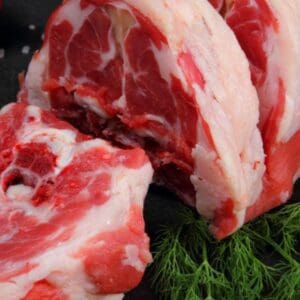 Raw marbled meat on dark surface, cut open; fresh dill, coarse salt, tomato in background.