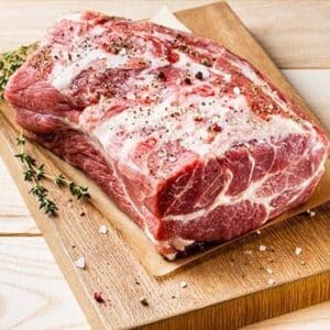 Raw seasoned pork roast on cutting board with thyme, salt, and pepper. Marbled texture.