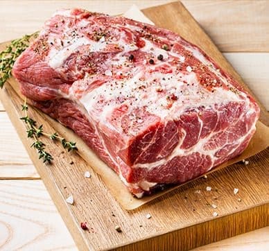 Raw seasoned pork roast on cutting board with thyme, salt, and pepper. Marbled texture.