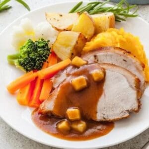 Plate with roast meat, gravy, mashed potatoes, roasted wedges, broccoli, carrots, cauliflower.
