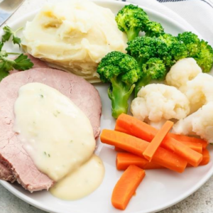 Plate with roast meat, creamy sauce, mashed potatoes, broccoli, cauliflower, carrot sticks.