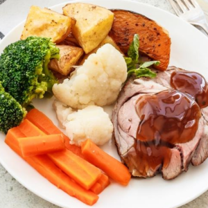 Plate with sliced roast meat, gravy, potatoes, sweet potato, broccoli, cauliflower, carrots.