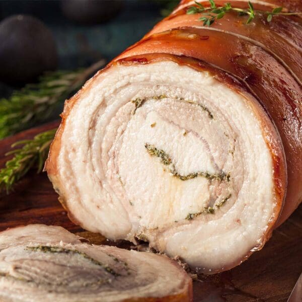 Roasted Porchetta Spiral on Board Rolled roasted porchetta with herbs on wooden board, crispy golden-brown exterior.