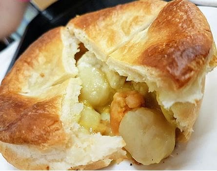 Savory golden-brown pastry with seafood and vegetable filling in creamy sauce, partially cut.