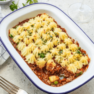 Shepherd's pie with mashed potatoes and herbs in a rectangular dish, fork nearby.