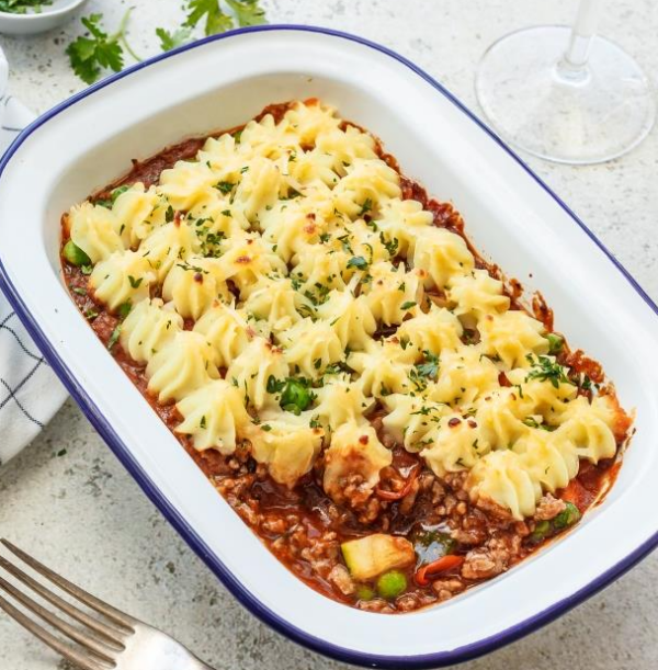 Shepherd's pie with mashed potatoes and herbs in a rectangular dish, fork nearby.
