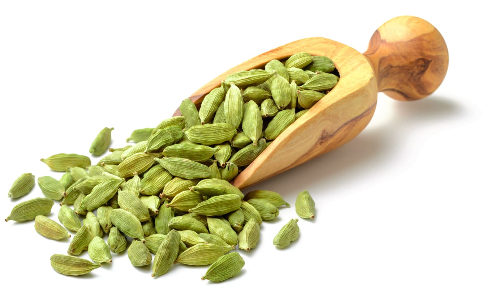 Wooden spoon with green cardamom pods on scattered white surface.