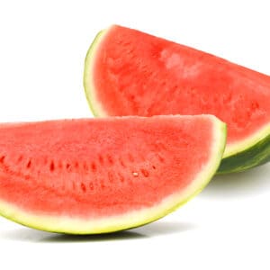 Whole watermelon and slices on white surface, green exterior, red interior with seeds.