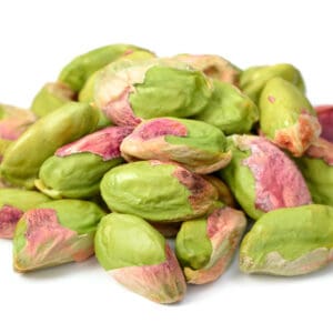 Cluster of unshelled pistachios on a white background, showing green and purple hues.