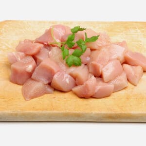 Raw cubed chicken breast on a wooden board with parsley garnish.