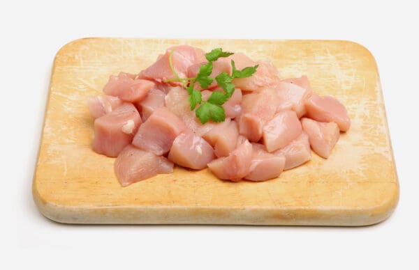 Raw cubed chicken breast on a wooden board with parsley garnish.