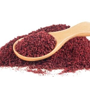 Wooden spoon with red spice on a white surface.