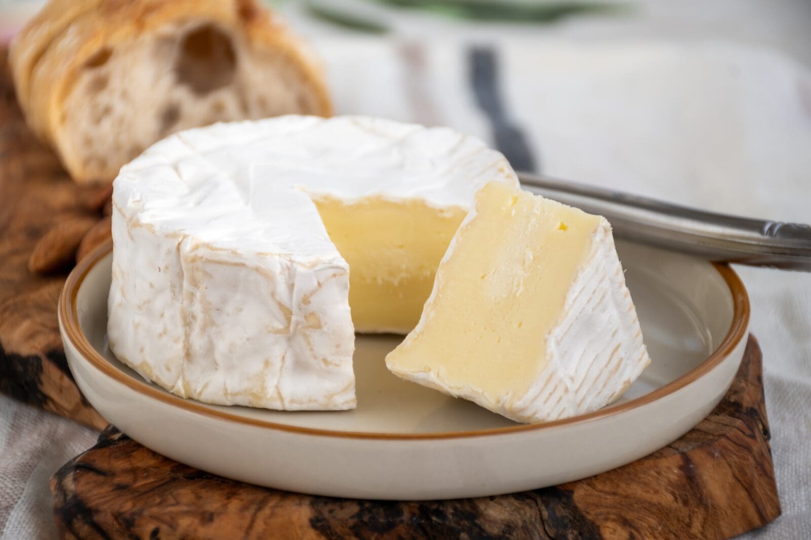 Soft cheese wheel with white rind, sliced to show creamy inside, on checkered cloth with honey.