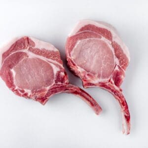 Two raw pork chops with bones displayed on a white surface.